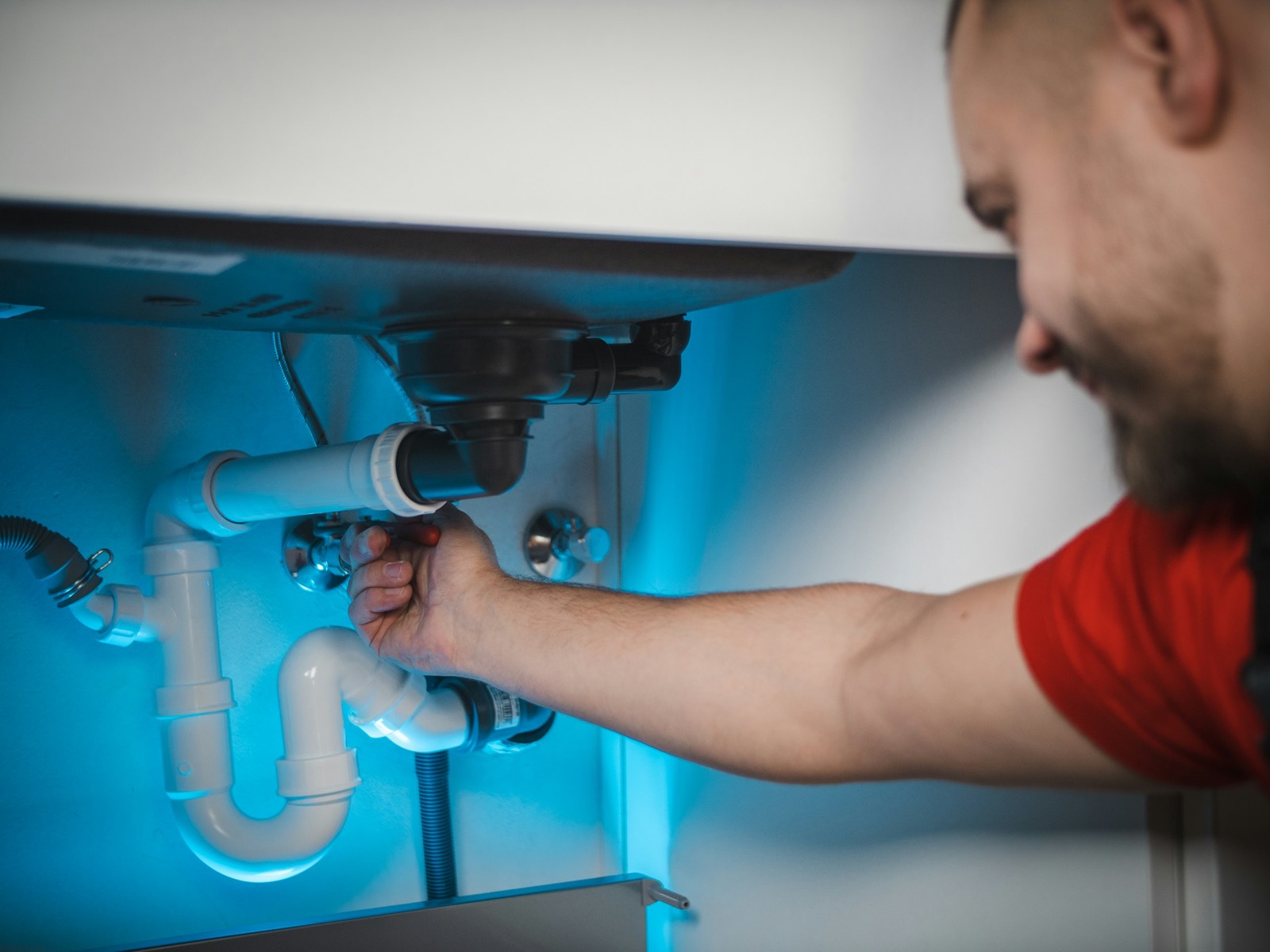 A plumber repairing pipework underneath a sink